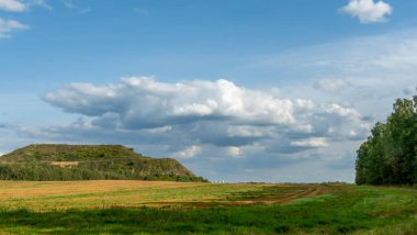 Kapalı şehir çöplüğü. Bölgenin restorasyonu. Büyük bir çöp yığınının peyzajı. Arka planda bir metropol ve bulutlu mavi bir gökyüzü var..