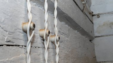 Beyaz ahşap bir duvardaki seramik yalıtkanlar üzerinde klasik stil bir elektrik kablosu. Elektrik bağlantı eklentisi çok eski elektrik hatları ve izolatörlerle kurulmuş..