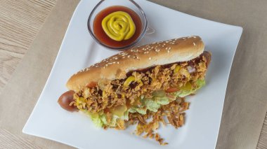 Marullu sosisli, turşulu, kızarmış soğanlı, beyaz tabakta ketçaplı. Danimarka malzemeleriyle hazırlanmış sosisli sandviç. Fast food kavramları.