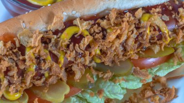 Marullu sosisli, turşulu, kızarmış soğanlı, beyaz tabakta ketçaplı. Danimarka malzemeleriyle hazırlanmış sosisli sandviç. Fast food kavramları.