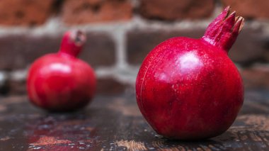 Masada iki kırmızı nar yatıyordu. Kırmızı tuğla duvarlı arka planda masada iki tane olgun taş var. Tüylü yemek. Hayat konsepti.