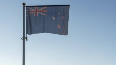 Yeni Zelanda 'nın ulusal bayrağı mavi gökyüzünün önündeki bayrak direğinde güneş ışınları ve lenslerle parlıyor. Diplomasi konsepti. Uluslararası ilişkiler. Metin için boşluk.