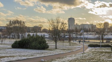 İlk kar şehirdeki yerleşim yerlerini kaplıyor. Güneş ışığı ve bulutlu gökyüzü. Şehir kavramları. Arka planda yüksek binalar var..