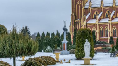 Kış çimenliği, köyde thuja ağaçları ve park heykelleri var. Peyzaj tasarımı. Bahçe kavramları. Arka planda eski bir kilise var..