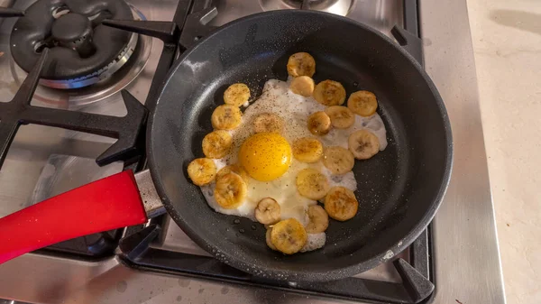 Cooking process of fried bananas with scrambled eggs. Fried Banana with eggs in hot pan. An exotic recipe for a sweet dish.
