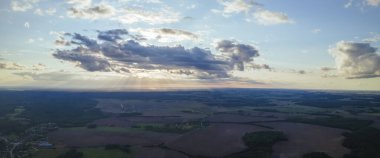 Yeşil tarlalar, orman ve yazın bulutlu mavi gökyüzü. Tarlaları, otları, ağaçları, güneşli gökyüzünü ve yemyeşil yapraklarını içeren soyut bir manzara. İnsansız hava aracıyla manzara.