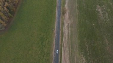 Kırsal yolda beyaz elektrikli arabanın hava manzarası. Kırsal kesimden geçen modern bir araç. Çevre dostu araba otoyol boyunca elektrik yükü ile gidiyor. Üst görünüm