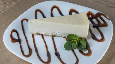 Beyaz tabakta nane yaprağı olan sade New York peynirli kek dilimi. Kahve molası kavramları. Yatay bileşim. Tasarım menüsü kafesi veya şekerlemesi için resim.