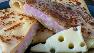 Peynir ve jambonla doldurulmuş krep. Siyah tabakta peynirli ve jambonlu krep. Doldurulmuş jambon ve peynirli krep. Sığ alan derinliği.