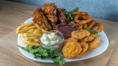Atıştırmalık tabaklar - peynir çubukları, tavuk nugget, soğan halkaları, patates kızartması ve soslar. Bira tahtası. Yatay fotoğraf. Bar menüsü için fotoğraf.