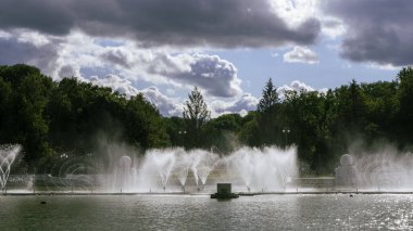 Çeşmeden su. Bulutlu gökyüzünün arkasındaki çeşme akıntısının tepesinde. Nehirdeki çeşme dramatik gökyüzüne karşı. Şehir manzarası görünümü.