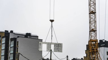 Kule vinci, bir inşaat alanının arka planına karşı monolitik bir bloğu kaldırıyor. Endüstri kavramları.