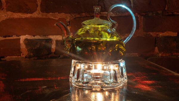 Boiling water and willow-herb or tea in a glass teapot. Red brick background.