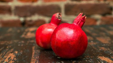 Masada iki kırmızı nar yatıyordu. Kırmızı tuğla duvarlı arka planda masada iki tane olgun taş var. Tüylü yemek. Hayat konsepti.
