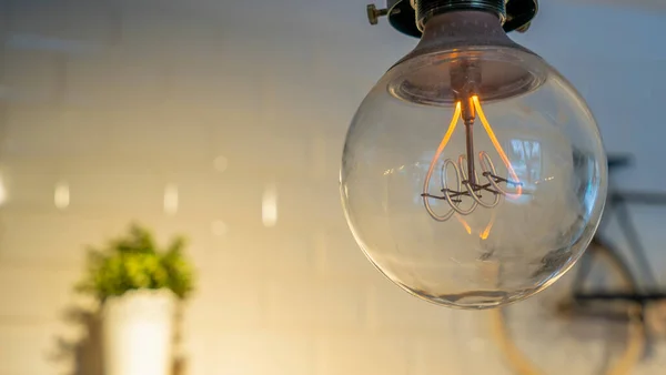 Verimli akkor ampul, fayanslı bir duvara karşı küçük bir bisiklet ve bir saksı ile elektrik israfı yapıyor. Dekoratif antika Edison ampulü. Metin için boşluk.