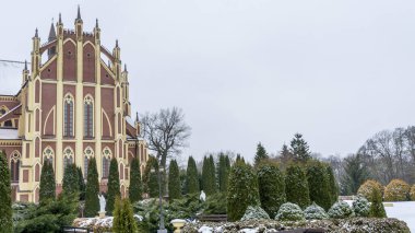 Kış çimenliği, köyde thuja ağaçları ve park heykelleri var. Peyzaj tasarımı. Bahçe kavramları. Arka planda eski bir kilise var..