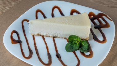 Beyaz tabakta nane yaprağı olan sade New York peynirli kek dilimi. Kahve molası kavramları. Yatay bileşim. Tasarım menüsü kafesi veya şekerlemesi için resim.