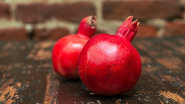 Masada iki kırmızı nar yatıyordu. Kırmızı tuğla duvarlı arka planda masada iki tane olgun taş var. Tüylü yemek. Hayat konsepti.