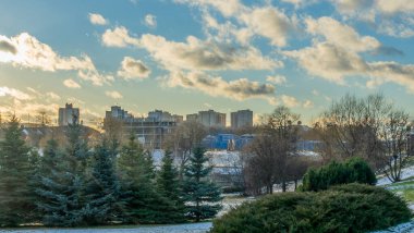 İlk kar şehirdeki yerleşim yerlerini kaplıyor. Güneş ışığı ve bulutlu gökyüzü. Şehir kavramları. Arka planda yüksek binalar var..