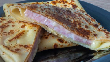 Peynir ve jambonla doldurulmuş krep. Siyah tabakta peynirli ve jambonlu krep. Doldurulmuş jambon ve peynirli krep. Sığ alan derinliği.