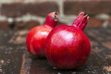 Masada iki kırmızı nar yatıyordu. Kırmızı tuğla duvarlı arka planda masada iki tane olgun taş var. Tüylü yemek. Hayat konsepti.