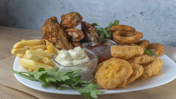 Atıştırmalık tabaklar - peynir çubukları, tavuk nugget, soğan halkaları, patates kızartması ve soslar. Bira tahtası. Yatay fotoğraf. Bar menüsü için fotoğraf.