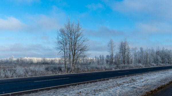 Загородная дорога через зимнюю сельскую местность. Черный чистый асфальт. Зимняя дорога проходит через заснеженные поля. Концепции транспортировки. Пространство для текста.