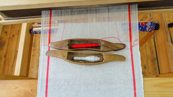 Wooden shuttle and spool on linen thread in the loom. Old shuttle loom made by wooden. Weaving shuttle on the linen fabric. Weaving tool and fabric on weaving machine.