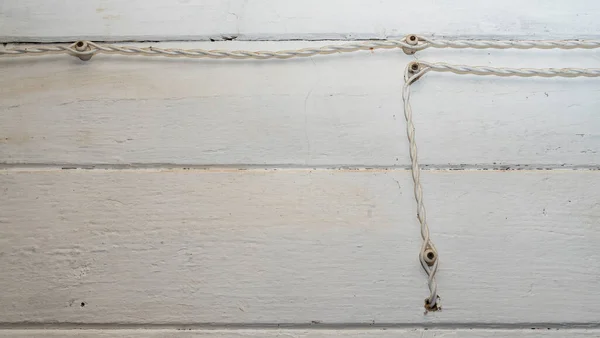 白い木製の壁にセラミック絶縁体上の繊維編組のヴィンテージスタイルの電気配線の断片 非常に古い電気線と絶縁体に設置された電気接合部 — ストック写真