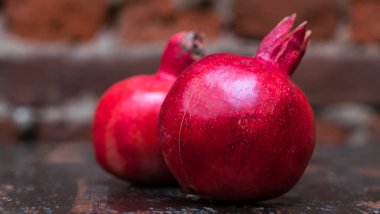 Masada iki kırmızı nar yatıyordu. Kırmızı tuğla duvarlı arka planda masada iki tane olgun taş var. Tüylü yemek. Hayat konsepti.