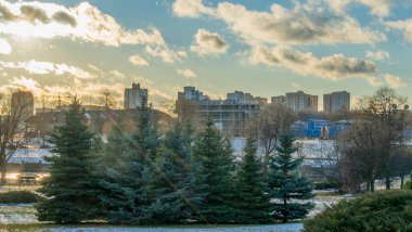 İlk kar şehirdeki yerleşim yerlerini kaplıyor. Güneş ışığı ve bulutlu gökyüzü. Şehir kavramları. Arka planda yüksek binalar var..