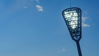 Spot ışıkları stadyumu aydınlatan direkler. Klasik mavi gökyüzü arkaplanı. Mesaj için yer var. Spor konsepti. Metin için boşluk.