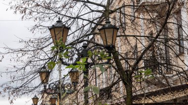 Mavi gökyüzü olan sokak lambası, arka planda ağaç dalları ve binalar. Karanlık gecede sokakları aydınlatmak için eski moda aydınlatma evi..