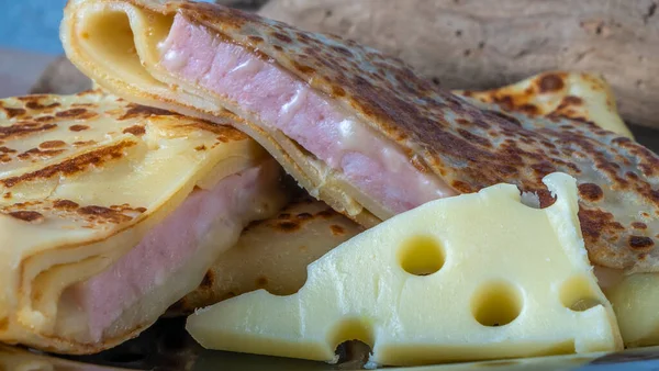 Crepe stuffed with cheese and ham. Pancake with cheese and ham on a black plate. Rolled pancakes stuffed ham and cheese. Shallow depth-of-field.