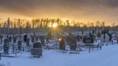 Karanlık mezar taşları ve ağaçlarla kaplı bir mezarlığın üzerinde kış günbatımı. Ölümden sonra. Samsara kavramları. Ölülerin dirileceği umudu. Metin için boşluk.