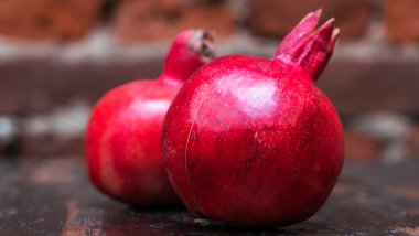 Masada iki kırmızı nar yatıyordu. Kırmızı tuğla duvarlı arka planda masada iki tane olgun taş var. Tüylü yemek. Hayat konsepti.