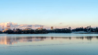 Kış bulutlu gökyüzüne karşı termik santralin bacalarını tüttürmek. Ekolojik sorunlar kavramı. Mesaj için yer var. Arka planda elektrik santrali olan gölün panoramik görüntüsü.