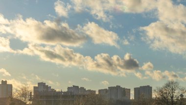 İlk kar şehirdeki yerleşim yerlerini kaplıyor. Güneş ışığı ve bulutlu gökyüzü. Şehir kavramları. Arka planda yüksek binalar var..