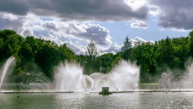 Çeşmeden su. Bulutlu gökyüzünün arkasındaki çeşme akıntısının tepesinde. Nehirdeki çeşme dramatik gökyüzüne karşı. Şehir manzarası görünümü.