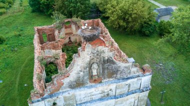 Genç leylekler harabe kilisesinin çatısındaki Katolik haçının yanındaki yuvada oturuyorlar. Hava görüntüsü. Doğa arkaplanı.