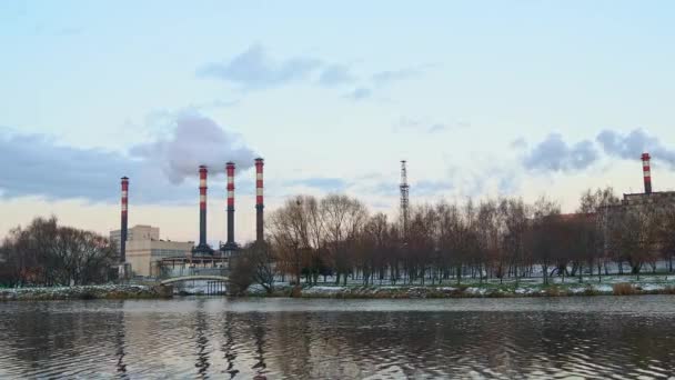 Továrna uprostřed města způsobující znečištění vzduchu v blízkosti vody. Tepelné elektrárny v zimě. Ekologické znečištění. Tovární trubky silný bílý kouř pára.