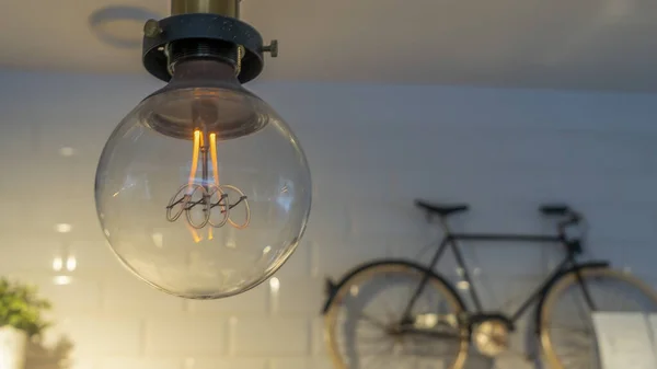 有效的白炽灯灯泡会把电浪费在用小自行车和花盆装饰的墙壁上 装饰古董爱迪生灯泡 案文的篇幅 — 图库照片