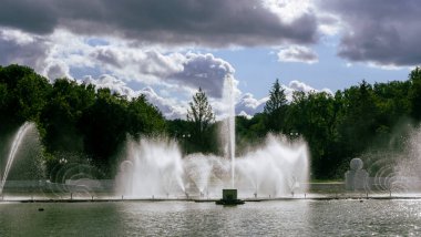 Çeşmeden su. Bulutlu gökyüzünün arkasındaki çeşme akıntısının tepesinde. Nehirdeki çeşme dramatik gökyüzüne karşı. Şehir manzarası görünümü.