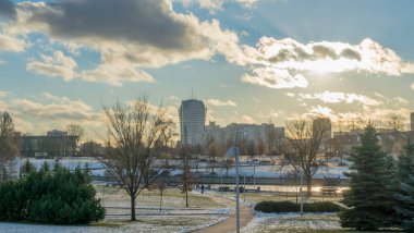 İlk kar şehirdeki yerleşim yerlerini kaplıyor. Güneş ışığı ve bulutlu gökyüzü. Şehir kavramları. Arka planda yüksek binalar var..