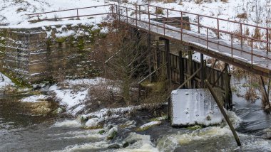 Kış nehri üzerindeki dar eski ahşap köprü. Kırsal kesimdeki nehir üzerinde tahta yaya köprüsü. Kış manzarası. Doğa kavramları.