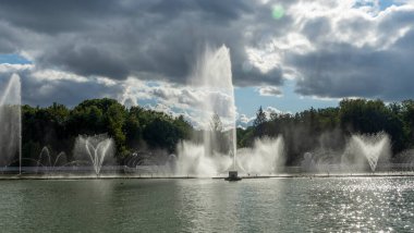 Çeşmeden su. Bulutlu gökyüzünün arkasındaki çeşme akıntısının tepesinde. Nehirdeki çeşme dramatik gökyüzüne karşı. Şehir manzarası görünümü.