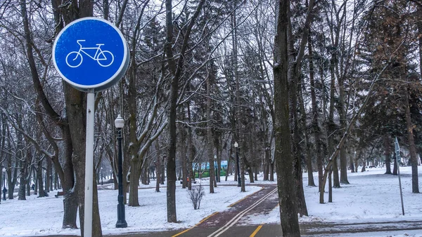 冬の公園で青い自転車レーンの標識 寒い気候でのサイクリング 寒い気候でのサイクリング 歩道上の自転車のステンシル 雪の降る冬の夜にサイクリング コンセプト交通標識 — ストック写真