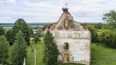 Genç leylekler harabe kilisesinin çatısındaki Katolik haçının yanındaki yuvada oturuyorlar. Hava görüntüsü. Hayvan teması.