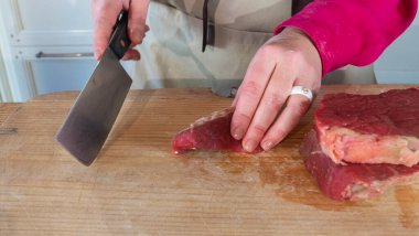 Bir kadın sulu bir parça et kesiyor. Et ve eller, yakın plan bıçakla. Kadın kesme tahtasındaki bıçakla bir parça et kesiyor..