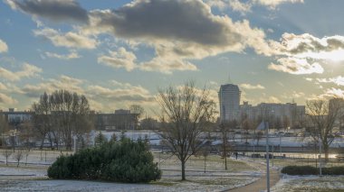 İlk kar şehirdeki yerleşim yerlerini kaplıyor. Güneş ışığı ve bulutlu gökyüzü. Şehir kavramları. Arka planda yüksek binalar var..